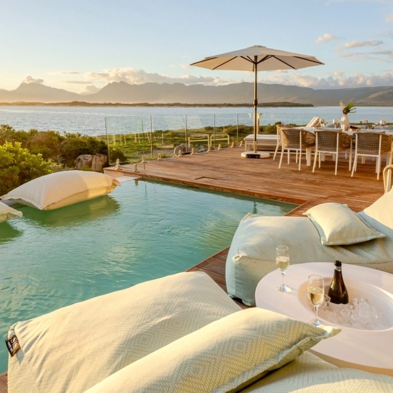Sundowners with a view — every evening a new show Glass-railed terrace at MBIZI lagoon house with panoramic views over Kleinrivier Lagoon, Hermanus